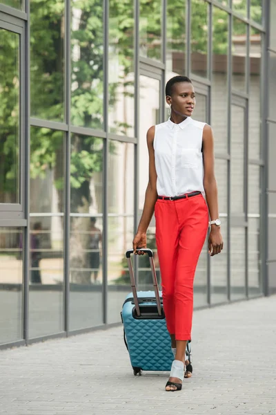 Elegante atractiva mujer de negocios afroamericana caminando con bolsa de viaje en la calle y mirando hacia otro lado - foto de stock