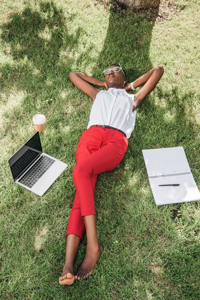 Високий кут зору стильна приваблива афроамериканська бізнес-леді лежить на траві в парку — стокове фото