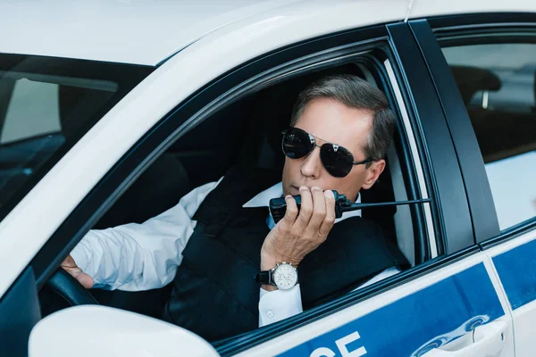 Middle aged male police officer in sunglasses talking on radio set in car — Stock Photo