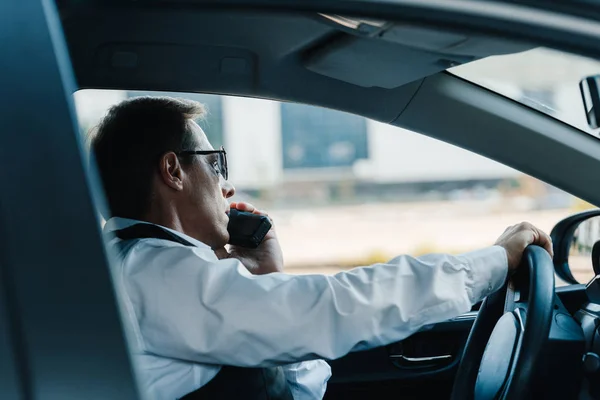 Seitenansicht eines reifen Polizisten mit Sonnenbrille, der im Auto im Radio spricht — Stockfoto