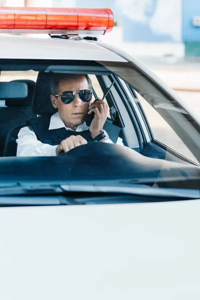 Policía de mediana edad en gafas de sol hablando por radio en el coche - foto de stock