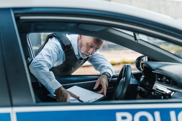 Mature policier dans gilet pare-balles prendre presse-papiers de voiture à la rue — Photo de stock