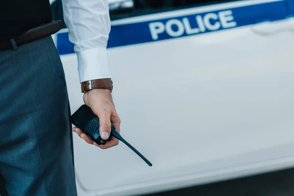Cropped image of policeman holding walkie-talkie near car at urban street — Stock Photo