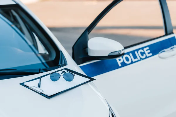 Blank clipboard with sunglasses on automobile with flasher and lettering police at city street — Stock Photo