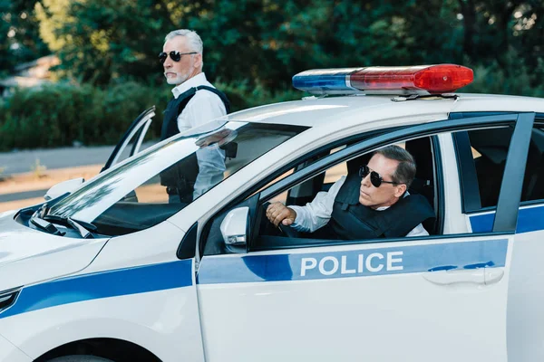 Oficiales de policía masculinos de mediana edad en gafas de sol saliendo del coche en la calle - foto de stock