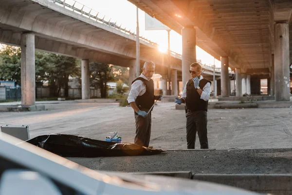 Policía de mediana edad en chaleco antibalas de pie cerca de colega mientras habla por radio en la calle de la ciudad - foto de stock