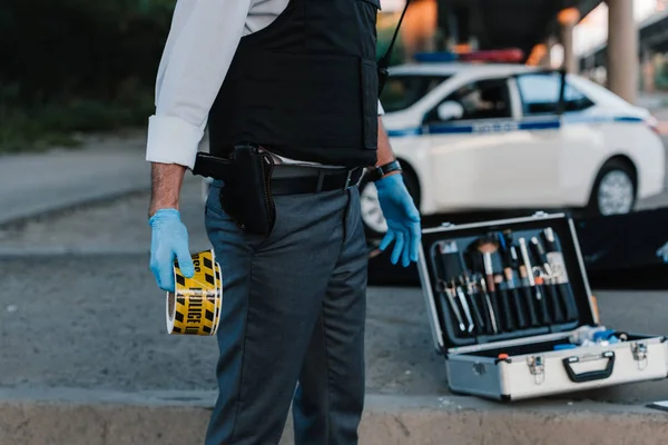 Image recadrée d'un policier portant des gants en latex tenant la ligne de police sur les lieux du crime — Photo de stock