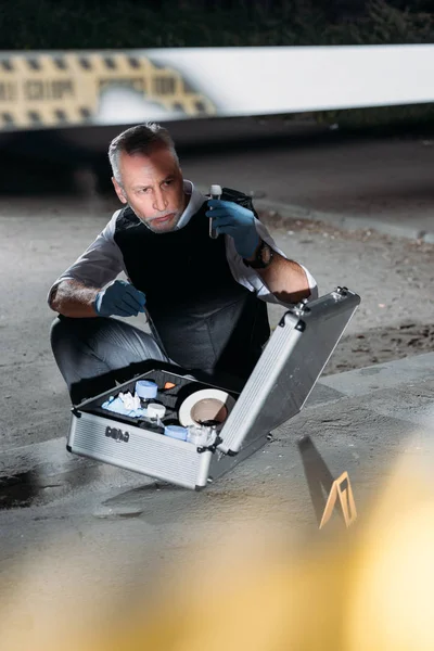 Middle aged male police officer collecting evidence near police line at crime scene — Stock Photo