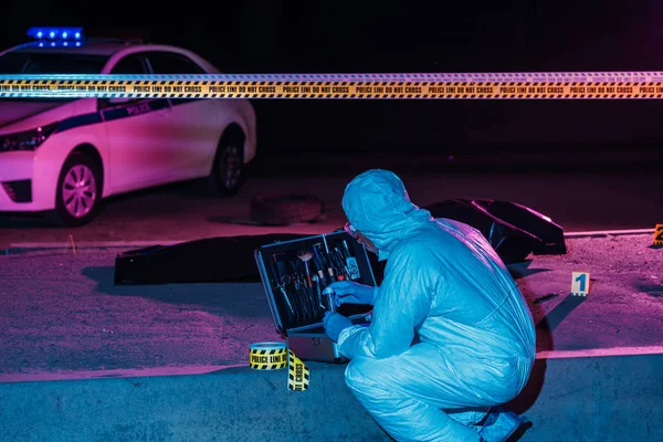 Rückansicht eines männlichen Kriminologen in Schutzanzug und Latexhandschuhen, der am Tatort mit Leiche Beweise sammelt — Stockfoto