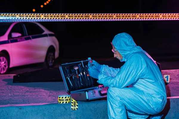 Criminologista maduro concentrado em terno protetor e luvas de látex coletando evidências na cena do crime com cadáver — Fotografia de Stock