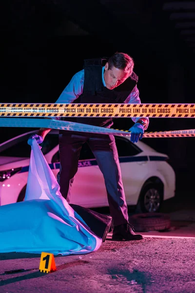 Polizist mittleren Alters sieht Leiche in Leichensack am Tatort — Stockfoto