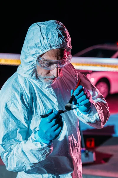 Criminólogo masculino en traje de protección y guantes de látex tomando huellas dactilares de cuchillo en la escena del crimen - foto de stock