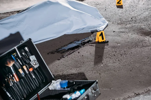 Vista de cerca del caso con herramientas de investigación y cadáver en bolsa de cadáveres en la escena del crimen - foto de stock