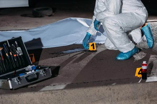 Cropped image of criminologist in protective suit and latex gloves collecting evidence at crime scene with corpse — Stock Photo