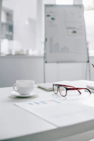 Cup of coffee and glasses on table in light modern office — Stock Photo