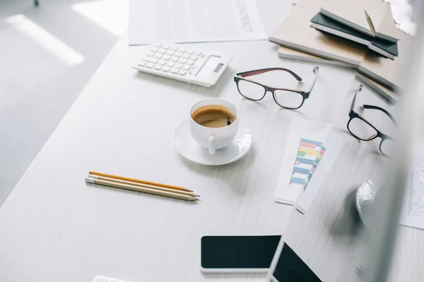 Vista de ángulo alto de la taza de café y vasos en la mesa en la oficina moderna luz - foto de stock