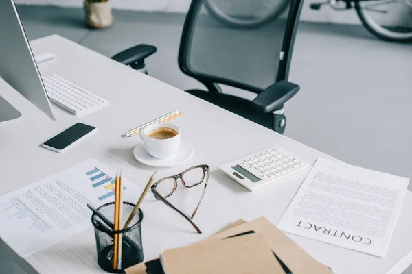 Vista de ángulo alto del titular de la pluma, taza de café y teléfono inteligente en la mesa en la oficina moderna luz - foto de stock