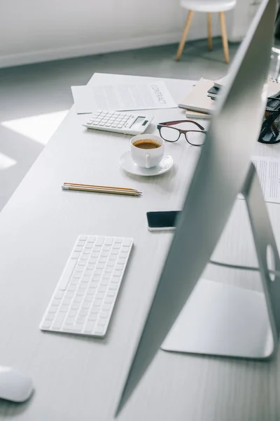 Computer, tazza di caffè e smartphone sul tavolo in leggero ufficio moderno — Foto stock