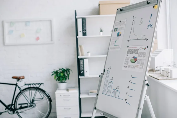 Tableau à feuilles mobiles avec stratégie de projet d'entreprise, vélo près du mur dans un bureau moderne léger — Photo de stock