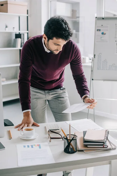 Красивый дизайнер в бордовом свитере читает документы в офисе — стоковое фото