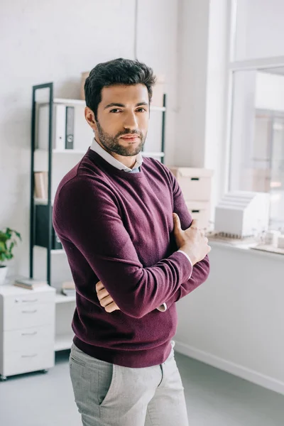 Schöne Designerin im weinroten Pullover mit verschränkten Armen im Büro vor der Kamera — Stockfoto