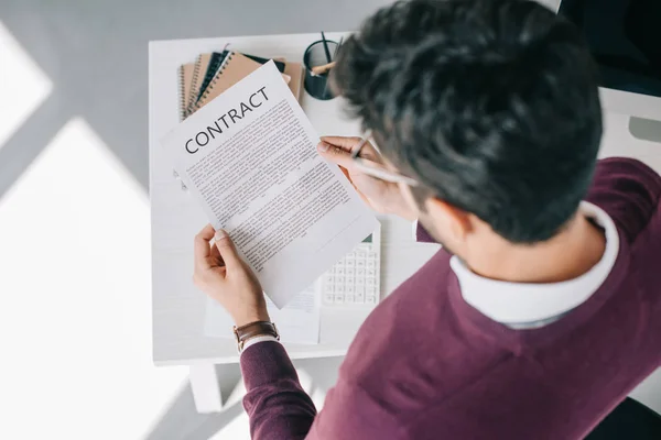 Overhead view of designer in burgundy sweater reading contract in office — Stock Photo