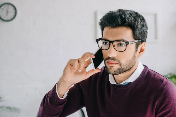 Portrait de beau designer dans des lunettes parlant par smartphone au bureau — Photo de stock