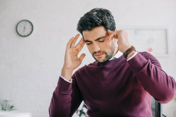Уставший бизнесмен в бордовом свитере с головной болью в офисе — стоковое фото