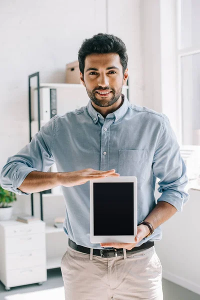 Apuesto arquitecto sonriente mostrando tableta con pantalla en blanco en la oficina - foto de stock
