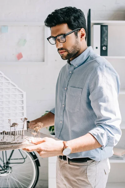 Seitenansicht eines hübschen Architekten, der ein Architekturmodell im Amt hält — Stockfoto