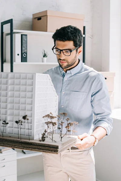 Gutaussehender Architekt hält und betrachtet Architekturmodell im Büro — Stockfoto