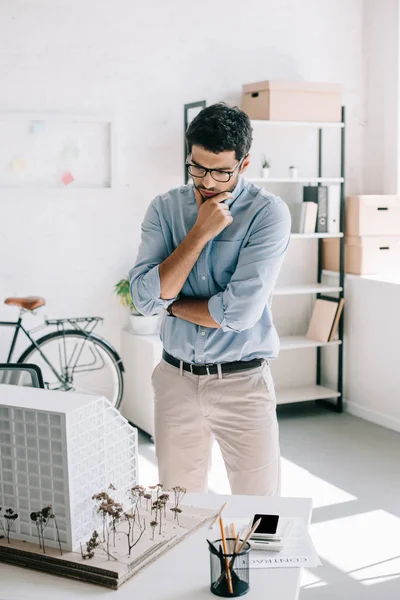 Pensive handsome architect looking at architecture model on table in office — Stock Photo