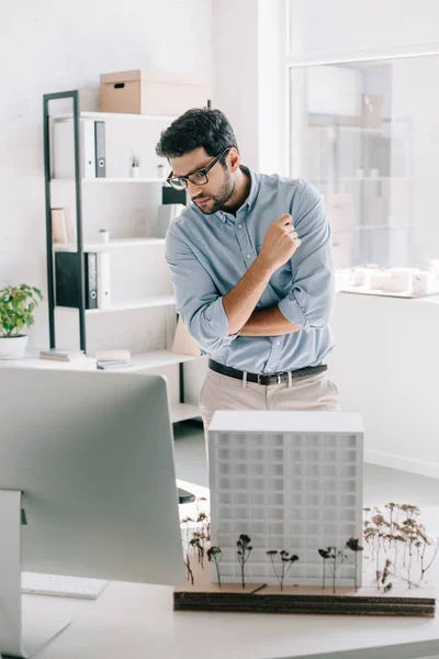 Красивый архитектор смотрит на компьютер рядом с архитектурной моделью на столе в офисе — стоковое фото