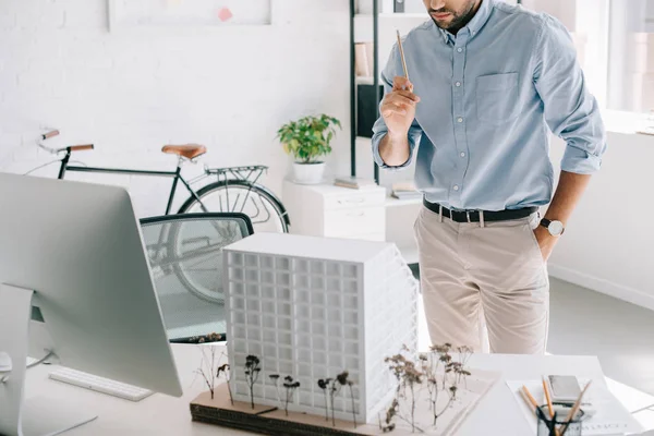 Cropped image of architect holding pencil and standing near architecture model on table in office — Stock Photo