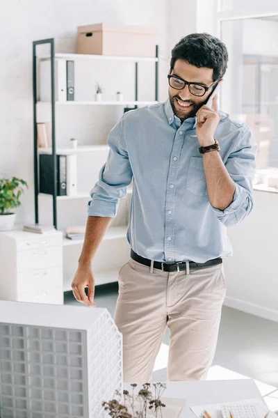 Красивый улыбающийся архитектор разговаривает со смартфоном в офисе — стоковое фото