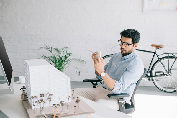 Schöner Architekt mit Smartphone-nahem Architekturmodell im Büro — Stockfoto