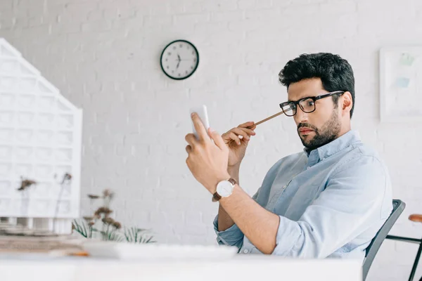 Architecte choqué en utilisant smartphone près du modèle d'architecture dans le bureau — Photo de stock