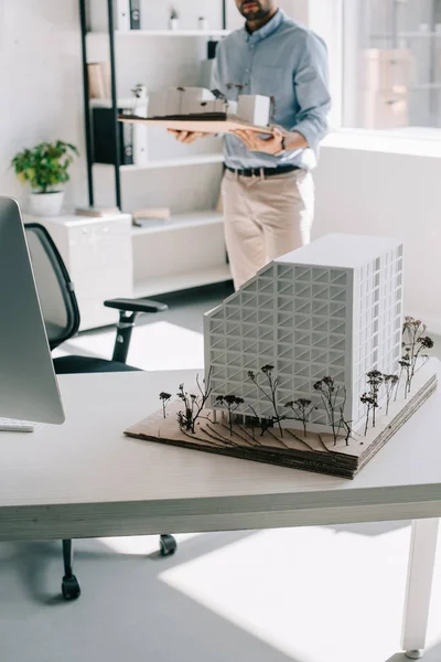 Обрезанный образ архитектора, держащего архитектурную модель в офисе — стоковое фото