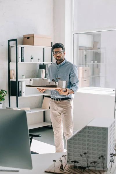 Handsome architect holding architecture model in office and looking at camera — Stock Photo