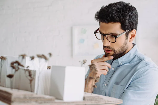 Handsome pensive architect in glasses looking at architecture model in office — Stock Photo