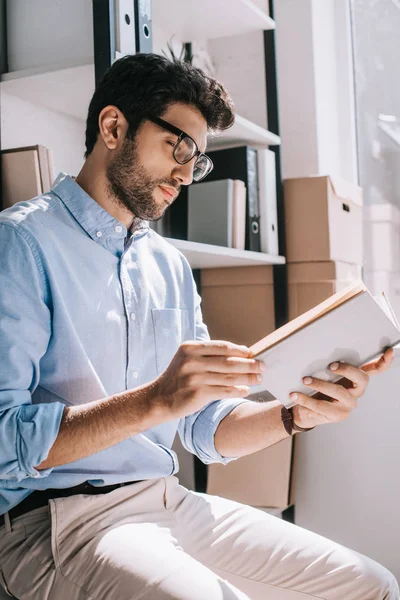 Side view of handsome architect in glasses reading book in office — Stock Photo