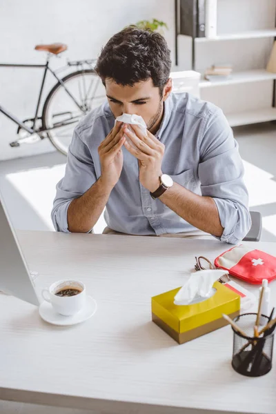 Sick businessman blowing nose in tissue in office — Stock Photo