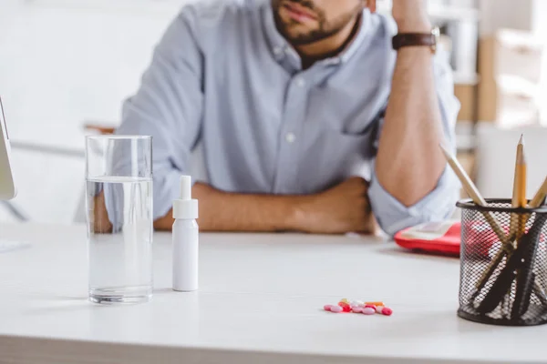 Обрізане зображення хворого менеджера, що спирається на стіл з ліками в офісі — стокове фото