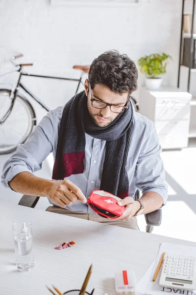 Kranker Geschäftsmann mit Schal öffnet Verbandskasten im Büro — Stockfoto