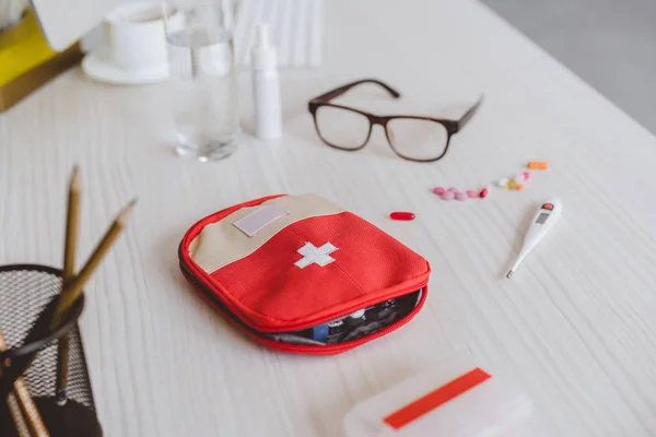 First aid kit, electronic thermometer and glasses on table in office — Stock Photo