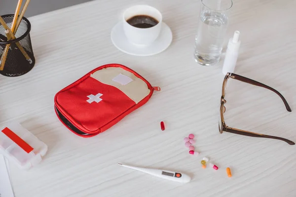 Аптечка, чашка кофе и таблетки на столе в офисе — стоковое фото