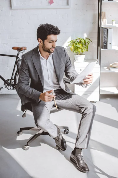 Gutaussehender Geschäftsmann liest Dokumente auf Stuhl im Büro — Stockfoto
