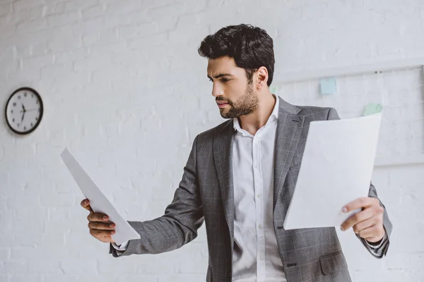 Seriöser gutaussehender Geschäftsmann liest Dokumente in leichtem Büro — Stockfoto