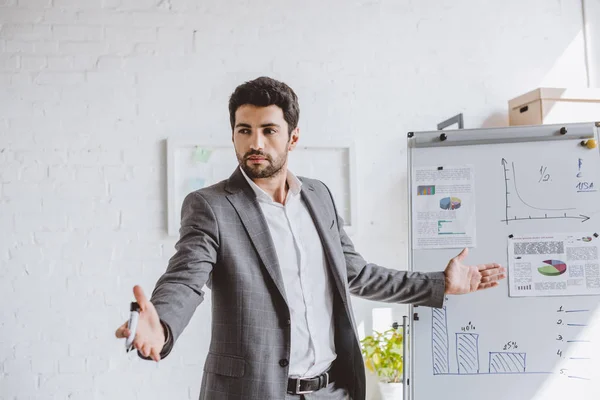 Handsome businessman presenting project on flipchart and gesturing in office — Stock Photo