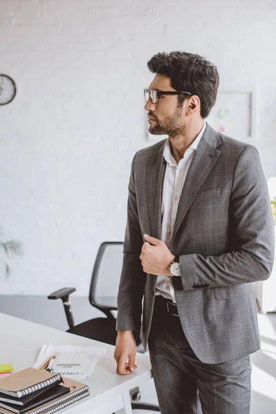 Guapo hombre de negocios de pie y mirando hacia otro lado en la oficina - foto de stock